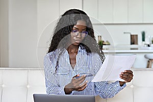 Young black woman holding paper working on laptop at home office.