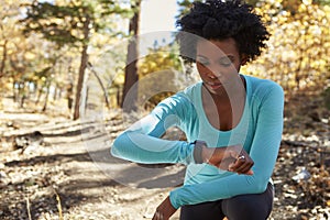 Young black woman kneeling in a forest checking smartwatch