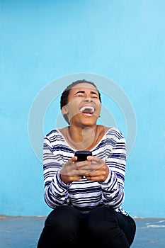 Young black woman laughing with cell phone against blue wall