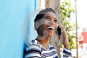 Young black woman leaning against wall and talking on mobile phone