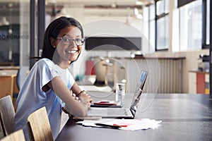 Young black woman in office with laptop smiling to camera