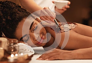 Young black woman receiving body scrub treatment at luxury spa