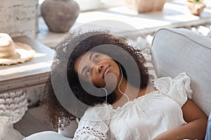Young black woman relaxing on comfortable couch, enjoying listening to lounge music