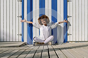 Young black woman on roller skates sitting near a beach hut.