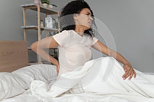 Young black woman sit on bed touching back feel backpain