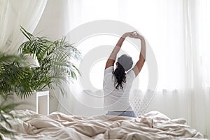 Young Black Woman Sitting In Bed And Stretching Arms After Waking Up