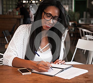 Young black woman sitting at cafe and writing notes, lifestyle concept