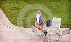 A young black woman is sitting on a chair by a green lawn, drinking coffee, taking a break