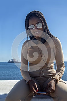 Young black woman smiling with headphones with blue sky and sea background