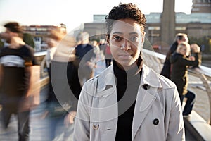 Young black woman standing on Millennium Bridge, London, looking to camera while pedestrians pass by, motion blur