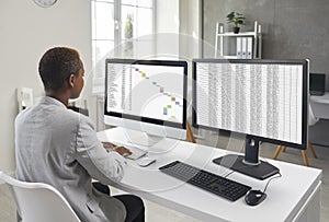 Financial accountant sitting at office desk and working on two desktop computers