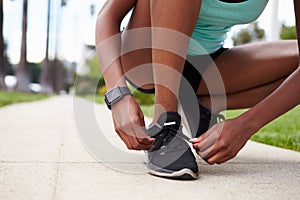 Young black woman tying sports shoes in the street