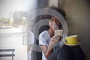 Young black woman using smartphone beside a window in a cafe