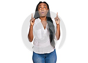 Young black woman wearing casual clothes amazed and surprised looking up and pointing with fingers and raised arms