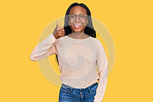 Young black woman wearing casual clothes and glasses smiling happy and positive, thumb up doing excellent and approval sign