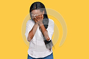 Young black woman wearing casual clothes with sad expression covering face with hands while crying