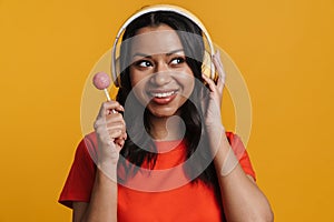 Young black woman wearing headphones smiling while holding lollipop