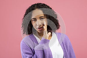 Young black woman whispering secret, sharing confidential information, spreading gossip on pink studio background