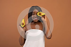 Young black woman wrapped in towel covering eye with avocado