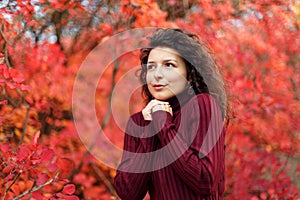Young blackhaired woman in red sweather heating her hands stay in red autumnn bushes
