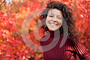 Young blackhaired woman in red sweather posing on camera in red autumnn bushes