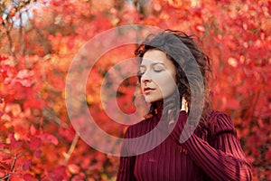 Young blackhaired woman in red sweather posing on camera in red autumnn bushes