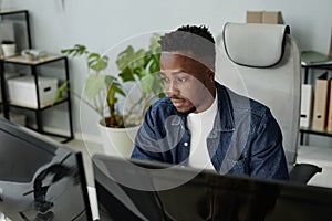 Young blackman in casual clothes sitting in front of computer monitors photo