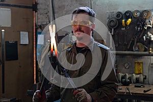 A young blacksmith is holding a red-hot workpiece with the help of pliers.