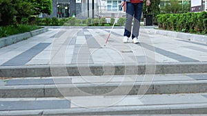 Young blind man with using safety stick for walking alone outdoors. Male person wearing glasses and casual clothes