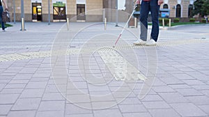 Young blind man with using safety stick for walking alone outdoors. Male person wearing glasses and casual clothes