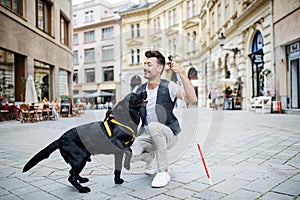 Young blind man with white cane and guide dog on pedestrain zone in city.