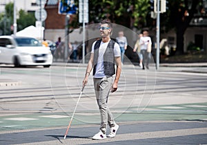 Young blind man with white cane walking across the street in city.