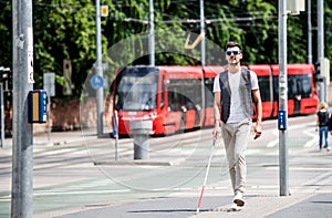 Young blind man with white cane walking across the street in city.