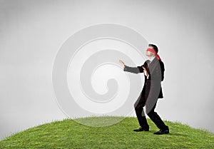 Blindfolded businessman steps on patch of grass