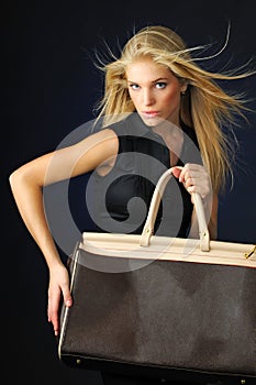 Young blond beautiful woman in black dress holding big leather bag in hands