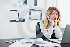 Young blond beautiful woman manager works in her modern office, holding her hands near face looks helpless and tired facing