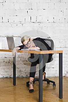 Young blond beauty businesswoman sitting at a office table with laptop, notebook and glasses in suit. Business concept.