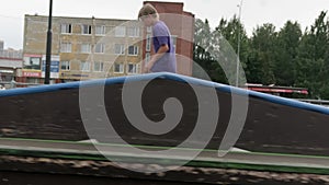 Young blond boy skateboarder rides forward on skateboard in skate park in cloudy weather. Professional skater teen