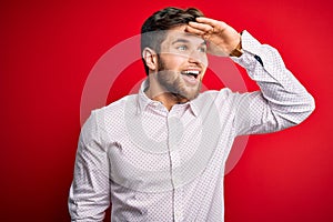 Young blond businessman with beard and blue eyes wearing elegant shirt over red background very happy and smiling looking far away
