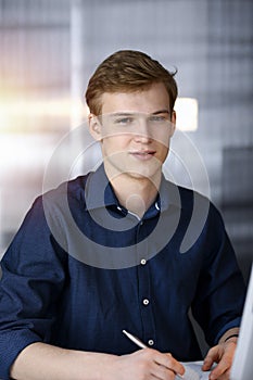 Young blond businessman working with computer in in a darkened office, glare of light on the background