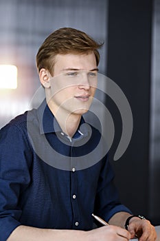 Young blond businessman working with computer in in a darkened office, glare of light on the background