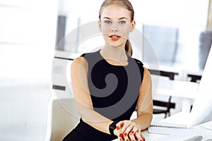 Young blond businesswoman working on computer while sitting at the desk in modern office. Business people concept. Black