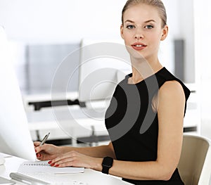 Young blond businesswoman working on computer while sitting at the desk in modern office. Business people concept