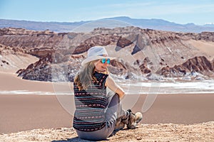 Young blond caucasian girl sitting and admiring outstanding landscape of untouched nature in Atacama desert, Chile