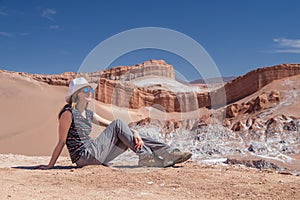Young blond caucasian girl sitting and admiring outstanding landscape of untouched nature in Atacama desert, Chile