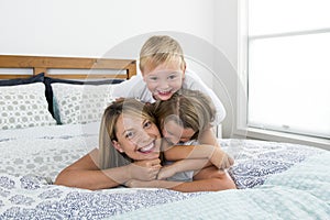 Young blond Caucasian woman lying on bed together with her little sweet 3 and 7 years old son and daughter laughing playing happy