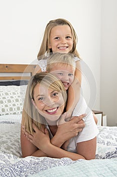 Young blond Caucasian woman lying on bed together with her little sweet 3 and 7 years old son and daughter laughing playing happy