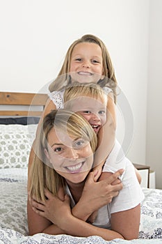 Young blond Caucasian woman lying on bed together with her little sweet 3 and 7 years old son and daughter laughing playing happy