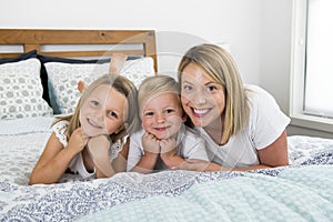 Young blond Caucasian woman lying on bed together with her little sweet 3 and 7 years old son and daughter smiling playful and hap