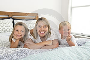 Young blond Caucasian woman lying on bed together with her little sweet 3 and 7 years old son and daughter smiling playful and hap
